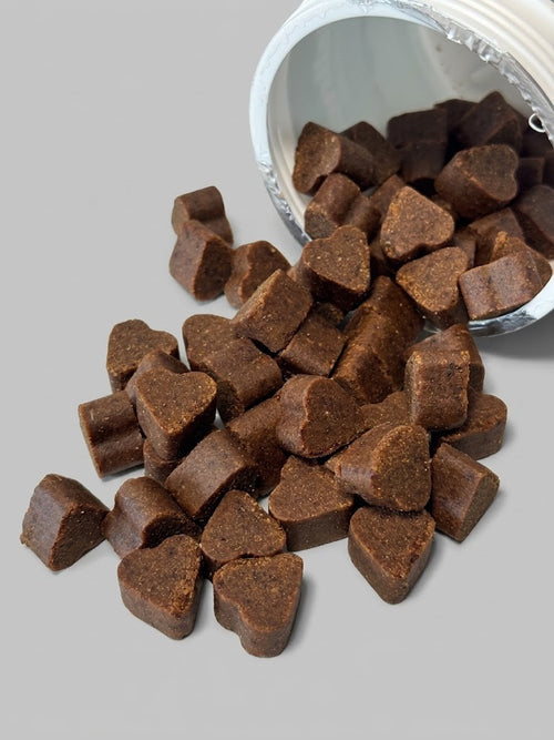 Heart-shaped brown dog treats spilling out of a container on a gray background